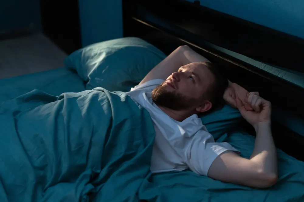 Тревожный мужчина лежит в кровати и смотрит в потолок.